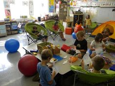 children are sitting around a table in a room with tents and balls on the floor