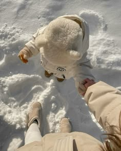 two people standing in the snow holding hands with a stuffed animal on top of them