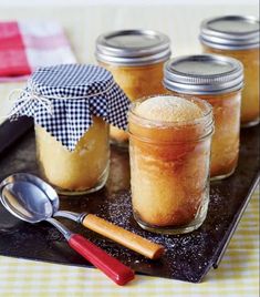 four jars filled with food sitting on top of a black tray next to a spoon