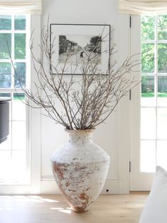 a white vase with branches in it sitting on the floor next to a couch and window