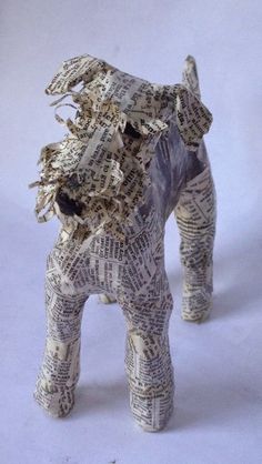 an origami dog made out of old newspaper pages is standing on a white surface