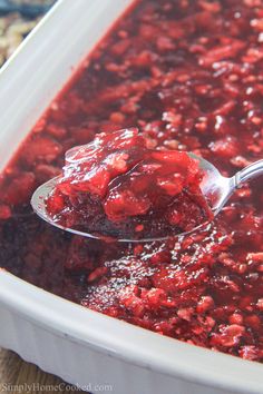 a spoon full of cranberry sauce on top of a white container with red stuff in it