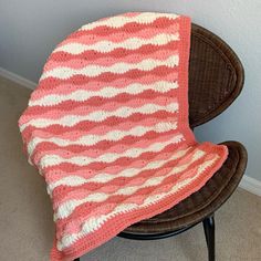 a pink and white crocheted blanket sitting on top of a chair next to a wall