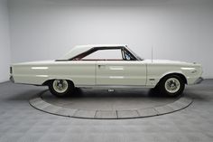 an old white car sitting on top of a circular display stand in a room with gray walls