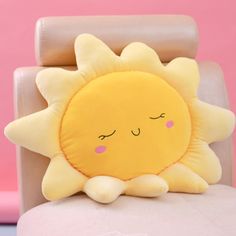 a yellow sun pillow sitting on top of a white chair next to a pink wall