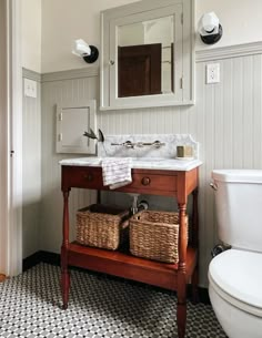 a white toilet sitting next to a bathroom sink under a mirror above a wooden vanity