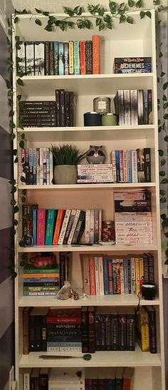 a bookshelf filled with lots of books next to a wall covered in ivy