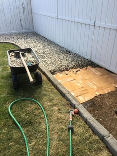 a wheelbarrow is sitting in the grass next to a garden hose and gravel