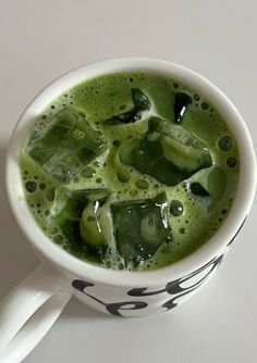 a cup filled with green liquid on top of a white table next to a spoon