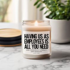 a candle that says having us as employees is all you need next to a potted plant