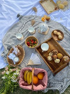 an outdoor picnic with fruit, pastries and tea on a blanket in the grass