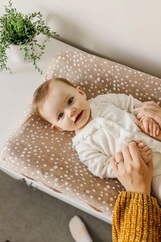 a woman holding a baby in her arms on top of a bed next to a potted plant