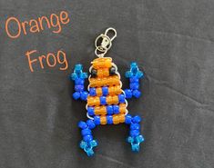 an orange and blue beaded frog sitting on top of a black surface next to the words orange frog