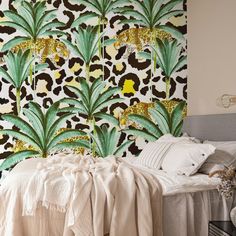 a bed sitting next to a wall covered in green and yellow leaves on top of it