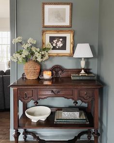 a wooden table topped with a vase filled with flowers next to a lamp and pictures on the wall