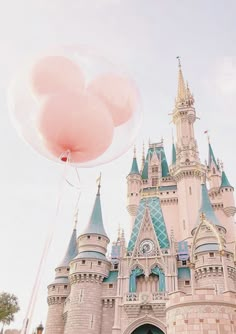 a pink balloon floating in front of a castle with two large balloons attached to it