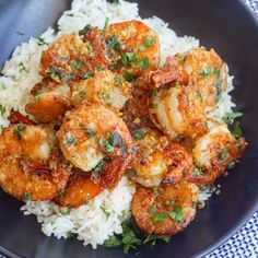 a black plate topped with rice and shrimp on top of a blue checkered table cloth