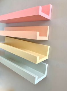 three shelves on the wall are painted different shades of pink, yellow and orange with white trim