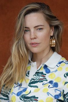 a woman with long blonde hair wearing large gold hoop earrings and a white button up shirt