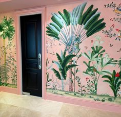 a pink room with green plants and flowers painted on the walls, along with a black door