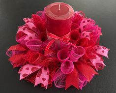 a red candle sitting on top of a pink and red mesh wreath with hearts around it