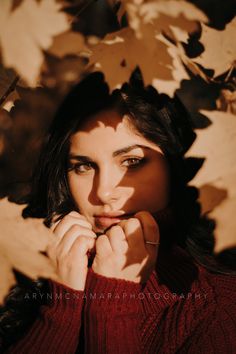 a woman is posing for a photo in front of some autumn leaves and has her hands on her face