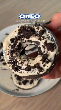 a person holding a chocolate doughnut with cream frosting and oreo on it