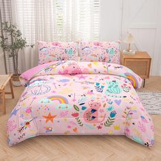 a bed with pink comforter and pillows on top of wooden floor next to window