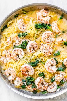 pasta with shrimp, spinach and cheese in a skillet on a marble surface