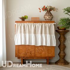 a vase with flowers on top of a wooden cabinet next to a plant and potted plants