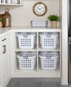 a kitchen with white cabinets and baskets in front of a clock on the wall above it