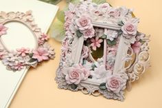 an ornate white frame with pink flowers on it next to a mirror and flower arrangement