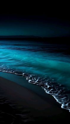 the ocean is blue and green with waves coming in to shore on a dark night