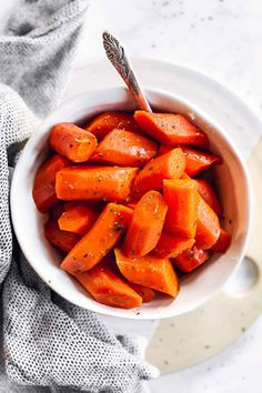 a white bowl filled with sliced carrots on top of a table next to a spoon