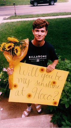 a young man holding a bouquet of sunflowers and a sign