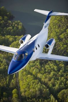 a blue and white plane flying over the trees in front of a body of water