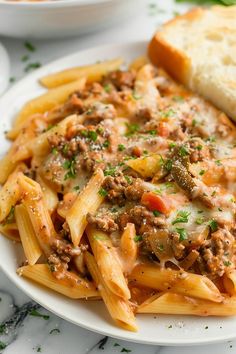 a white plate topped with pasta covered in meat and sauce next to bread on a marble table