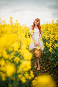 a woman with red hair is standing in a field full of yellow flowers and holding a basket