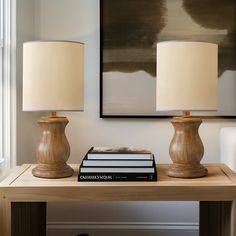 two lamps sitting on top of a wooden table next to a book and lamp shade