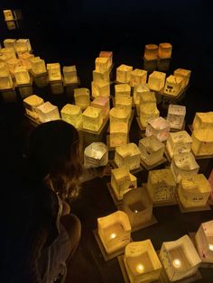 a woman sitting in front of many lit up boxes on the ground with candles around her