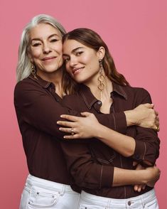 two women hugging each other in front of a pink background with their arms around one another