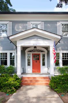 a red door sits in front of a gray house with white trim and two windows