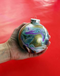 a hand holding a marbled ornament on a red surface