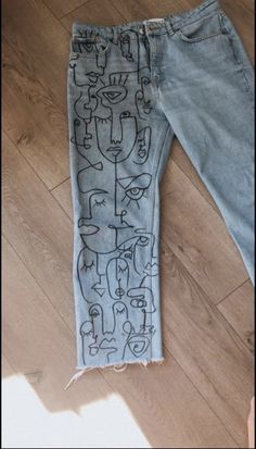 a pair of blue jeans with drawings on them sitting on the floor next to a wooden floor