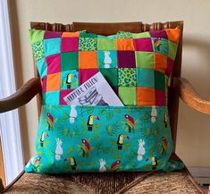 a colorful pillow sitting on top of a chair next to a wooden chair with a magazine in it