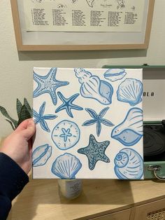 a person holding up a piece of paper with shells and starfishs on it