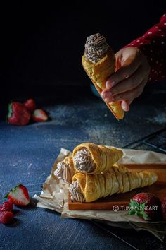 a person holding a pastry in their hand and some strawberries on the table next to it