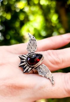 This unique garnet bat wing ring captures the essence of gothic elegance with its intricate design and striking appearance.   The centerpiece of the ring is a captivating garnet, known for its rich, deep red color and lustrous shine. Ring design size 1.8 inches wide × .9 inches long. Size 7. Ready to ship. Wing Ring, Gothic Elegance, Bat Wing, Deep Red Color, Statement Ring Silver, Intricate Design, Bat Wings, Deep Red, Sterling Ring