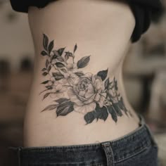 a woman's lower back tattoo with flowers on her stomach and leaves around the waist