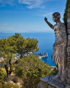 a statue on top of a stone wall next to trees and the ocean in the background